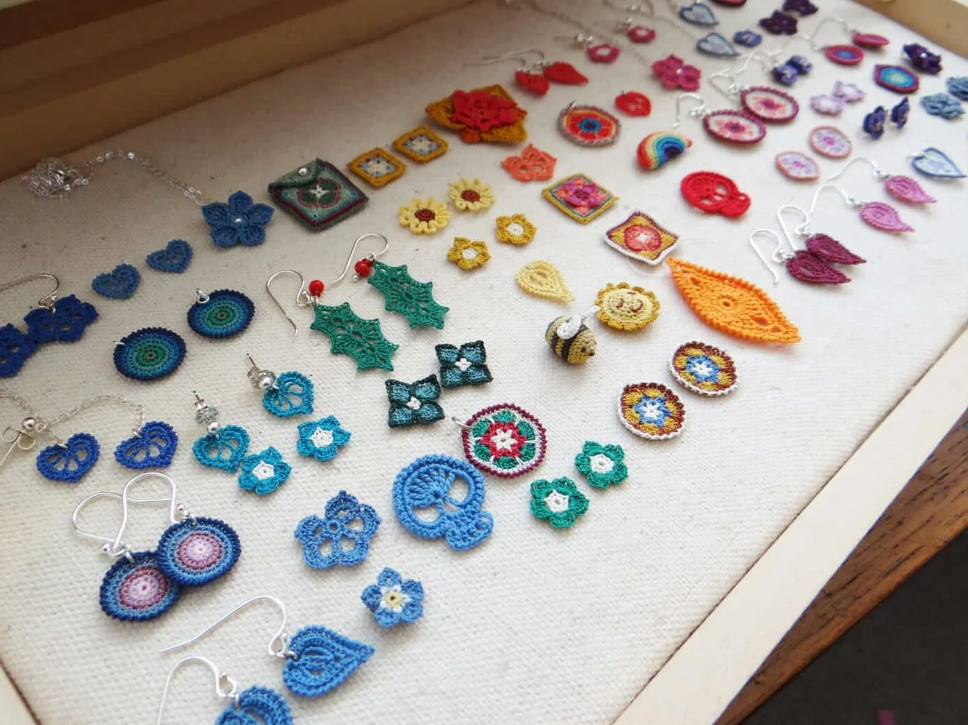 micro crochet earrings and motifs laid out in wooden presentation box, including holly leaves, granny squares, tiny flowers, skulls, bumble bees and more