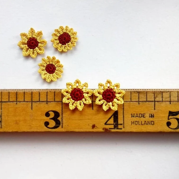 5 tiny micro crochet sunflowers on a vintage ruler